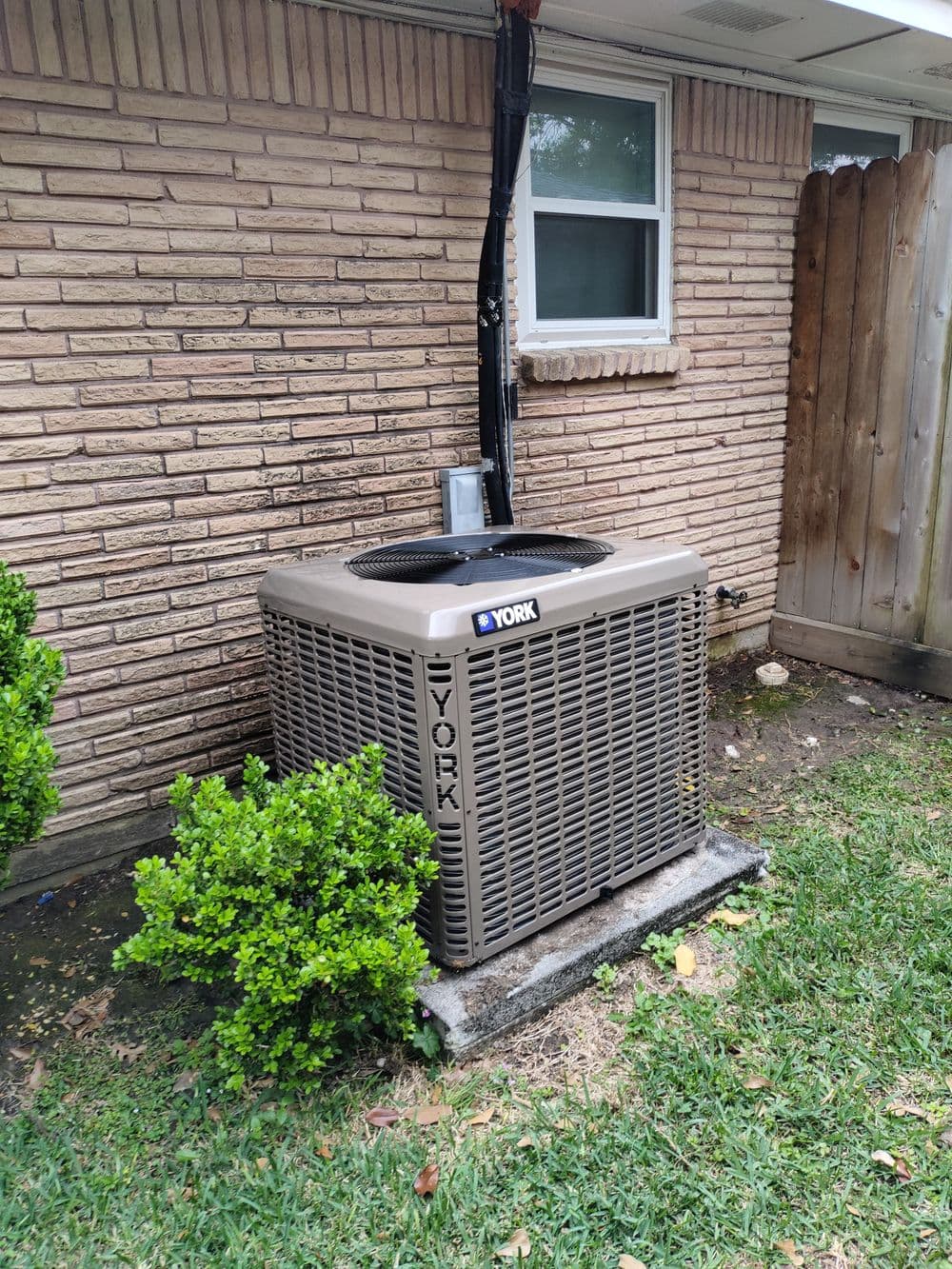York air conditioning unit beside a brick house with trimmed bushes and grass.