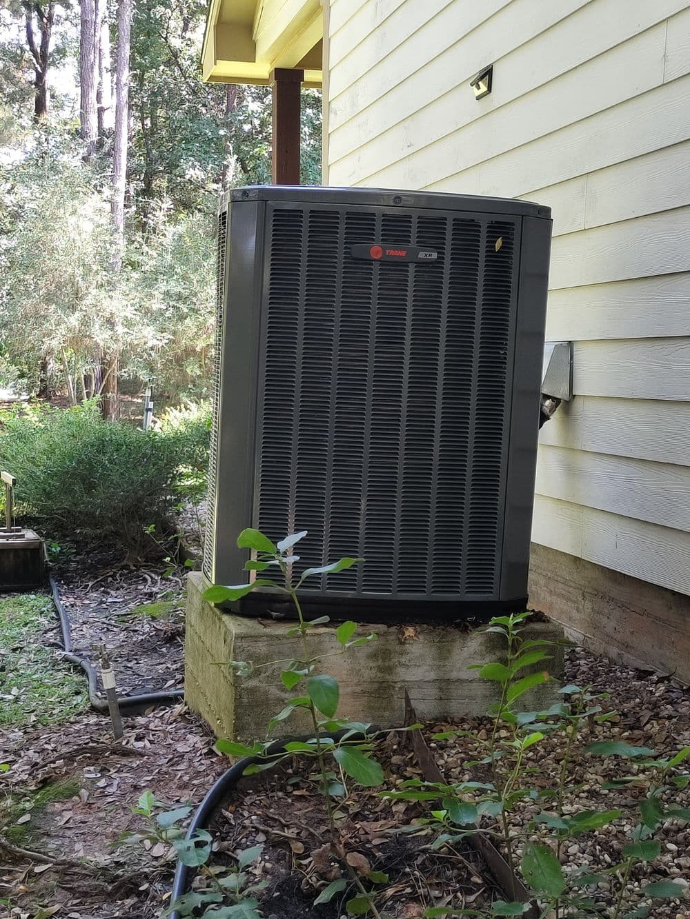 Trane air conditioning unit installed outside a home near a wooded area.