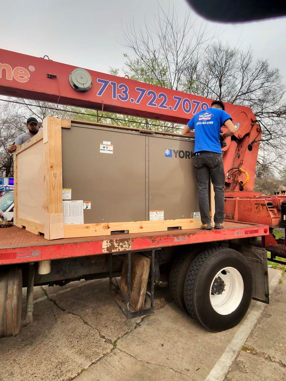 Technicians unloading a York HVAC unit from a truck during installation.