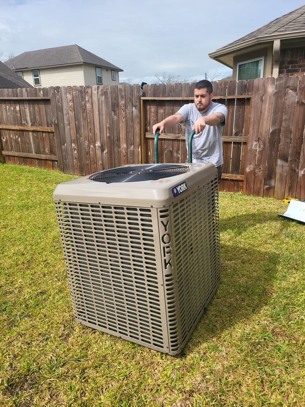 Technician installing a York air conditioning unit in a grassy yard.