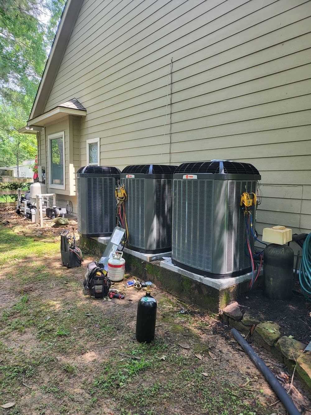 Three energy-efficient air conditioning units installed beside a house, surrounded by tools and equipment.