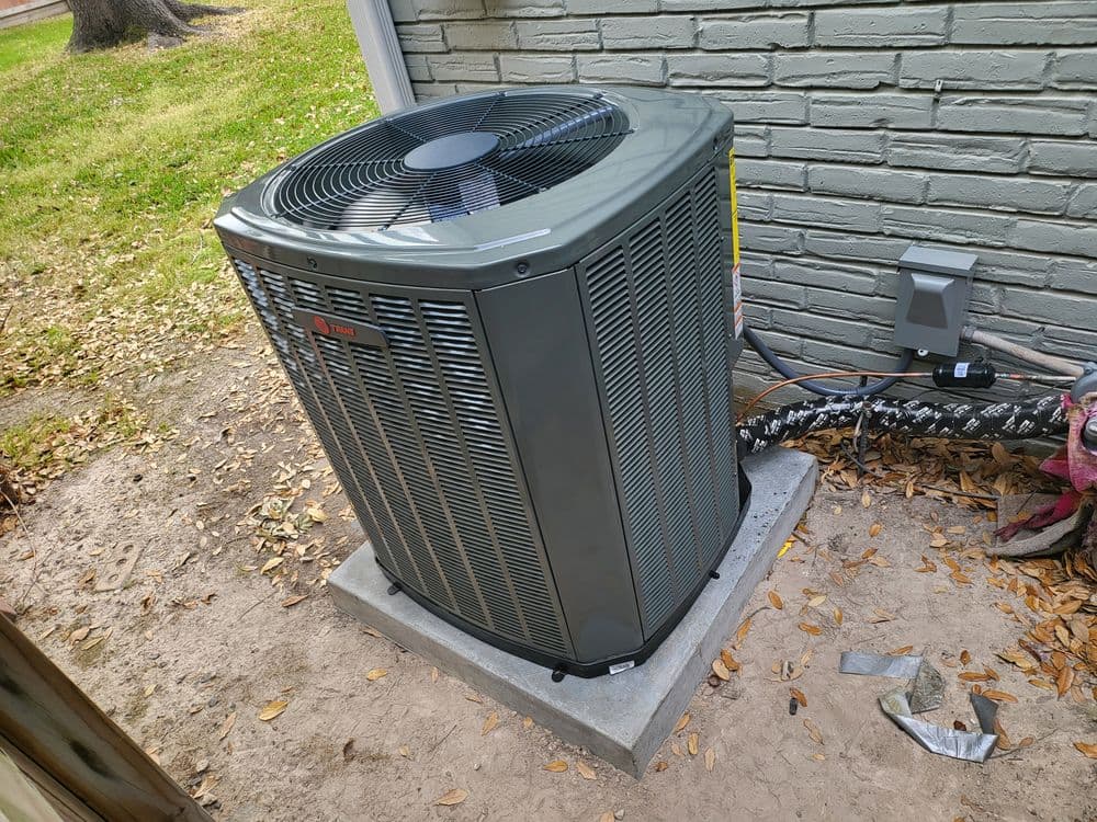 Modern outdoor air conditioning unit installed on concrete pad beside a house.