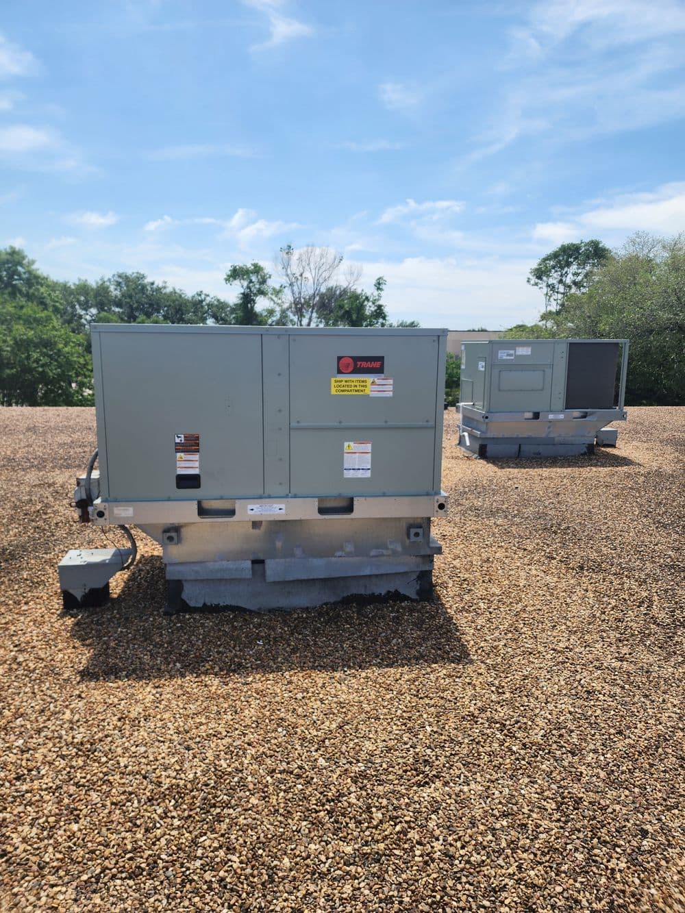 Two commercial HVAC units on a gravel rooftop under a clear blue sky.